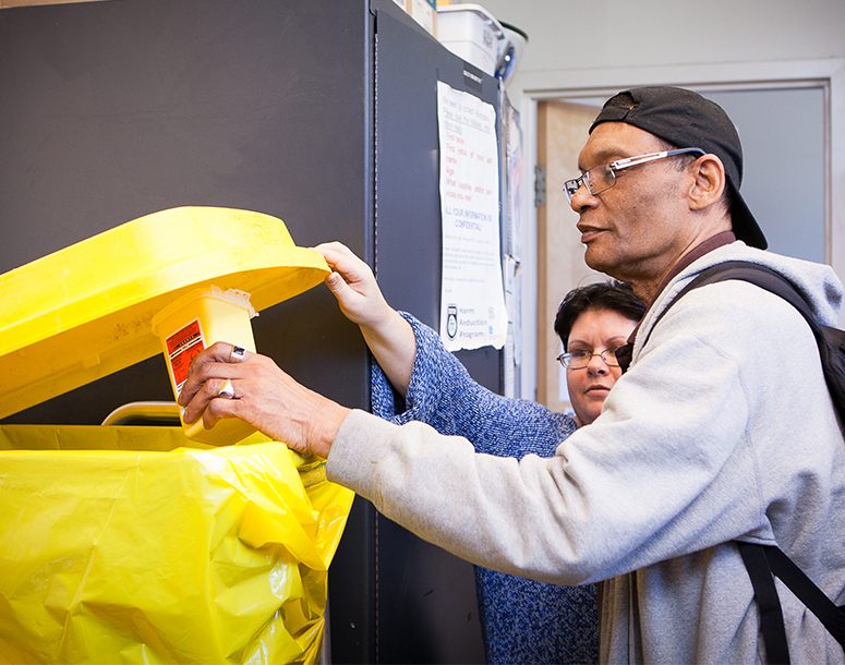 Man being assisted with placing object in a yellow bin