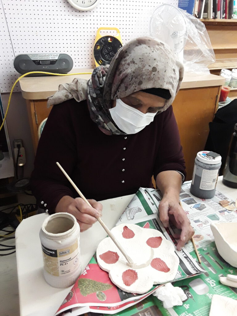 Woman painting her clay piece to get ready for firing