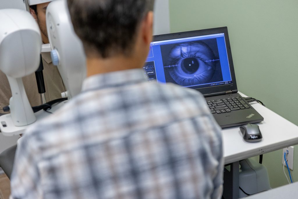 Looking over the shoulder at a laptop screen displaying a close-up view of an eye