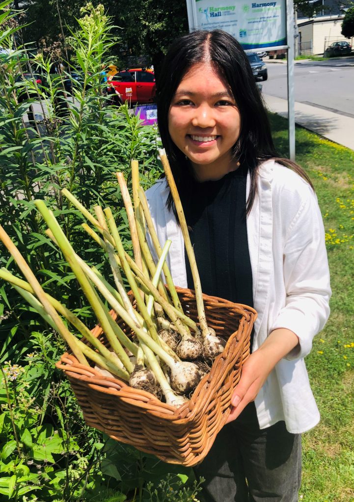 Young women stands outside holding a basket of fresh garlic