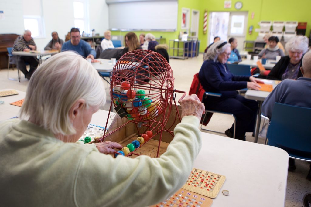 A woman is getting ready to call out a bingo number to a room full of seniors