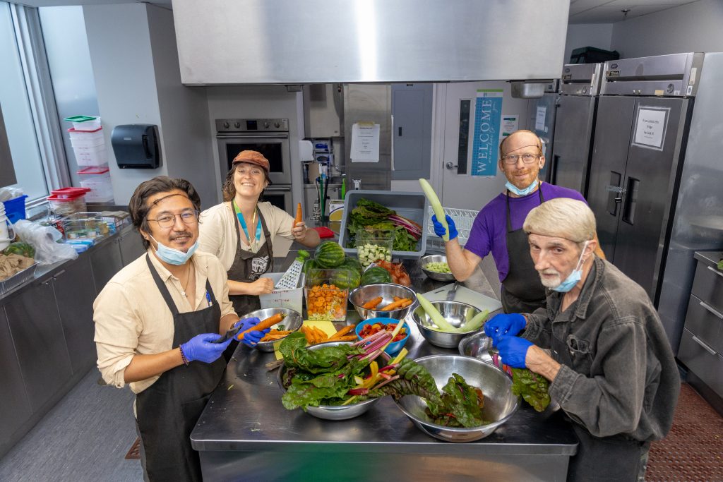 A group of four people stand in the Centre's kitchen, preparing food from a selection of fresh vegetables on a metal table
