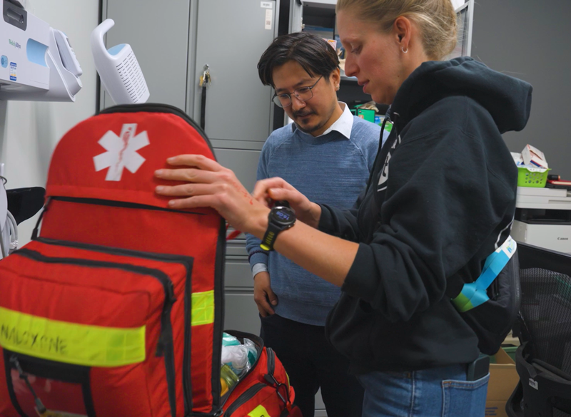 Two people stand and look at an open medical supply bag