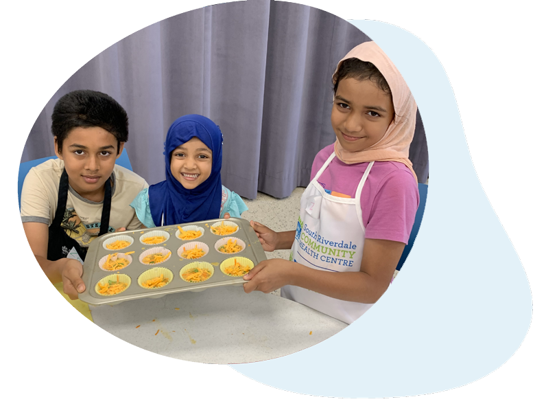 3 children pose with a muffin pan that is filled with food that is ready to go into the oven