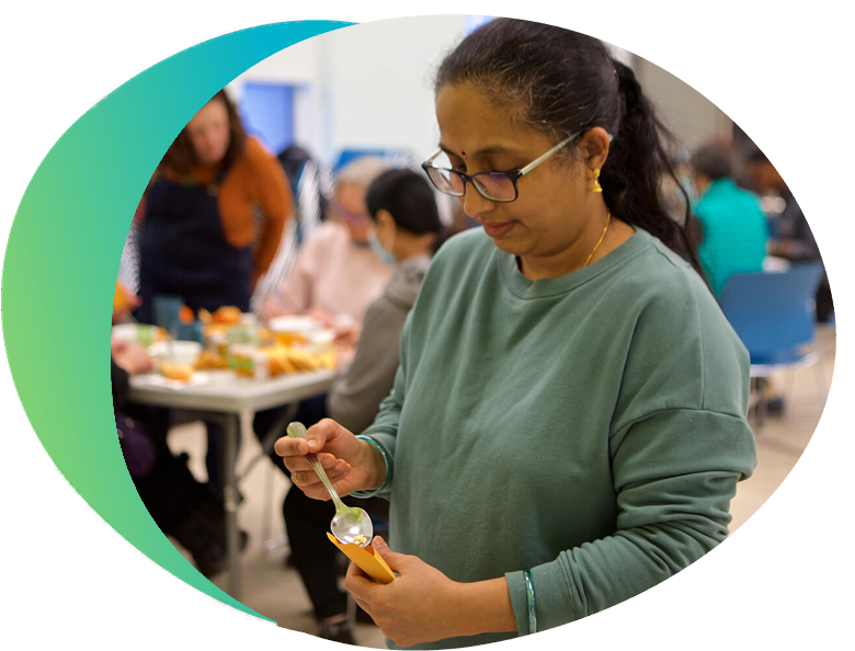 A woman is standing and holding a spoon to drop seeds into an envelope as part of a seed saving workshop