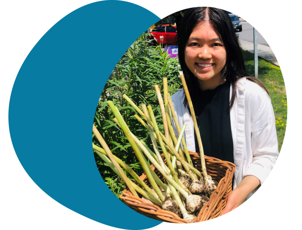 Young women stands outside holding a basket of fresh garlic