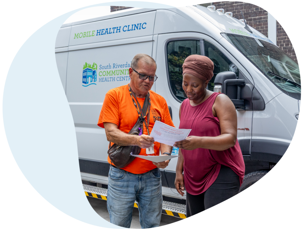 Two people look at a flyer while standing in front of a mobile clinic vehicle