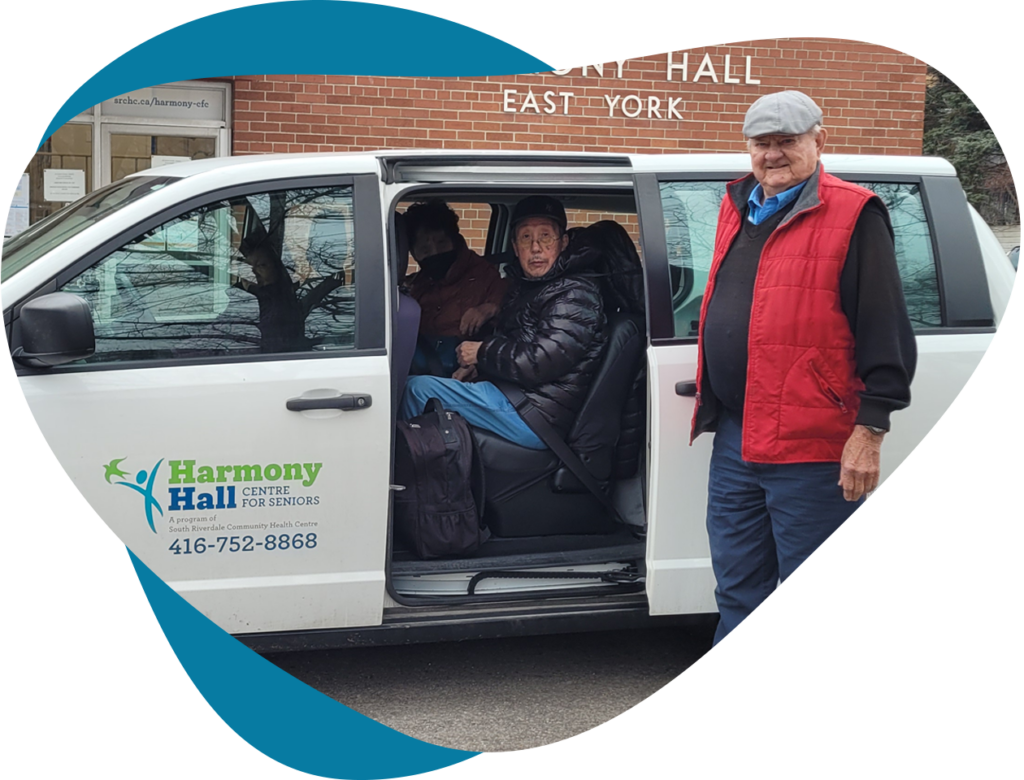 A person sits inside of a van with an open door. Next to the open door stands a Harmony Hall driver