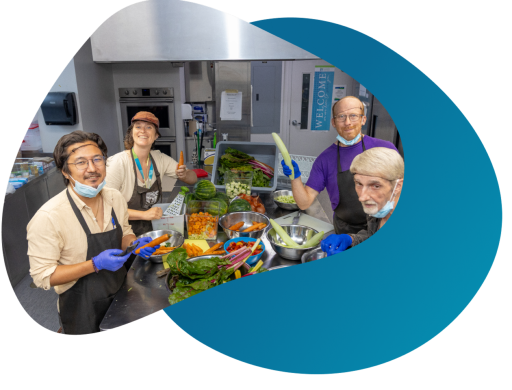 A group of four people stand in the Centre's kitchen, preparing food from a selection of fresh vegetables on a metal table